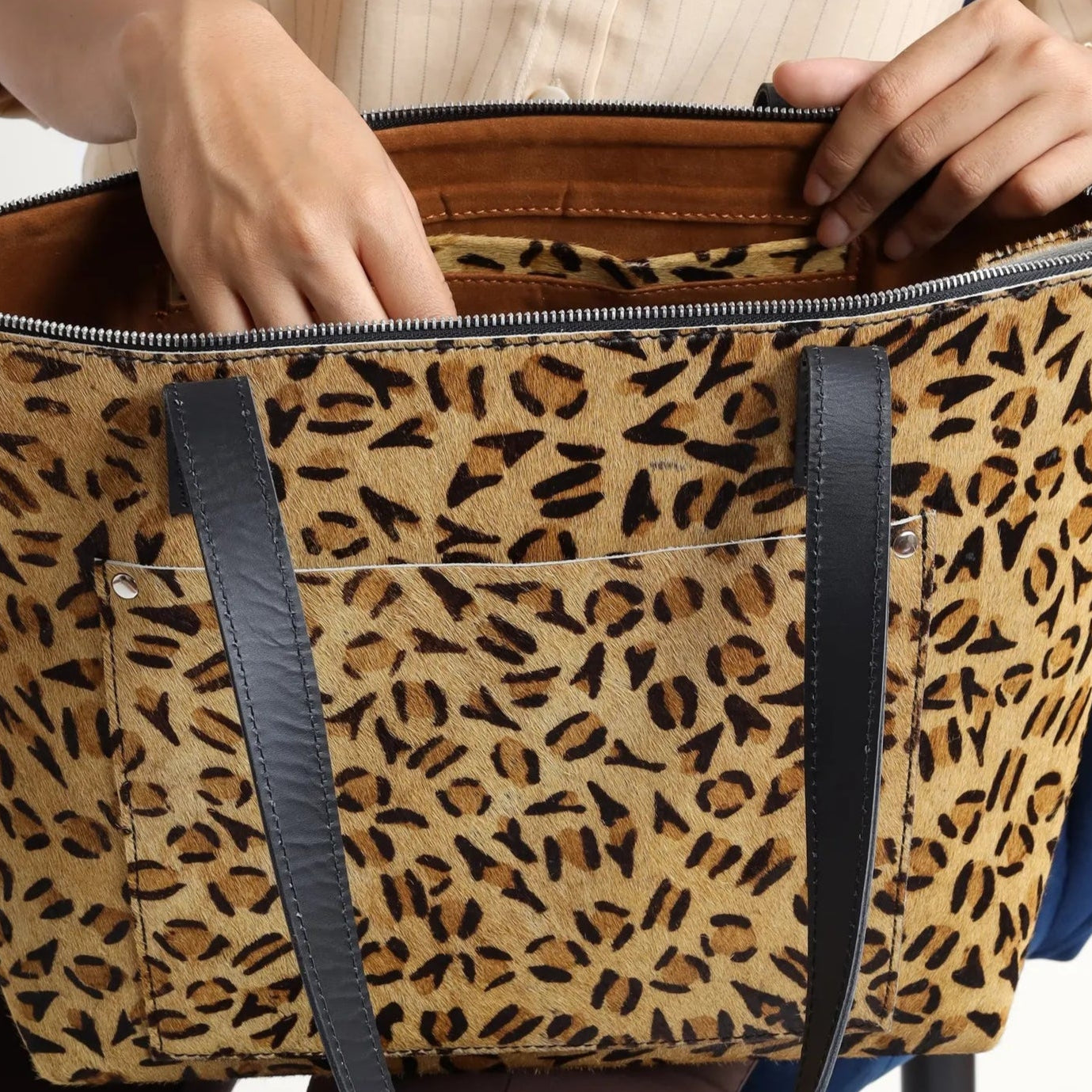 Person holding a leopard print bag with a visible brand logo on a plain background