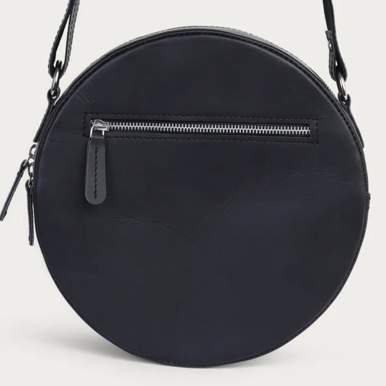 Black round crossbody bag with a strap on a light gray background