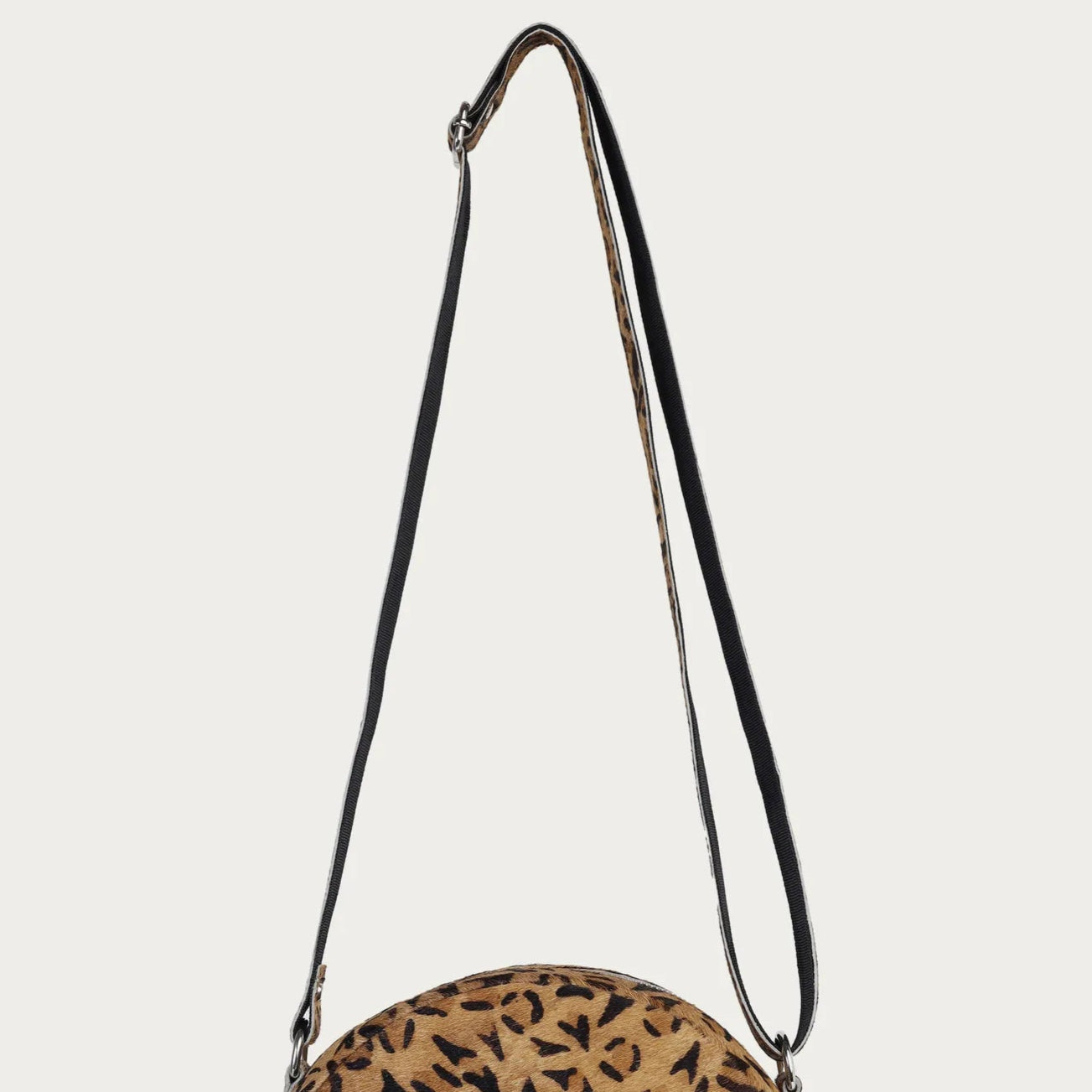 Round crossbody bag with leopard print pattern on a beige background