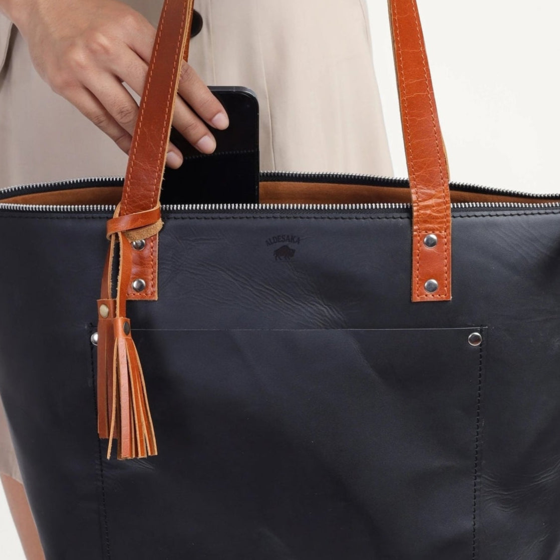 Person holding a black tote bag with brown handles against a white background