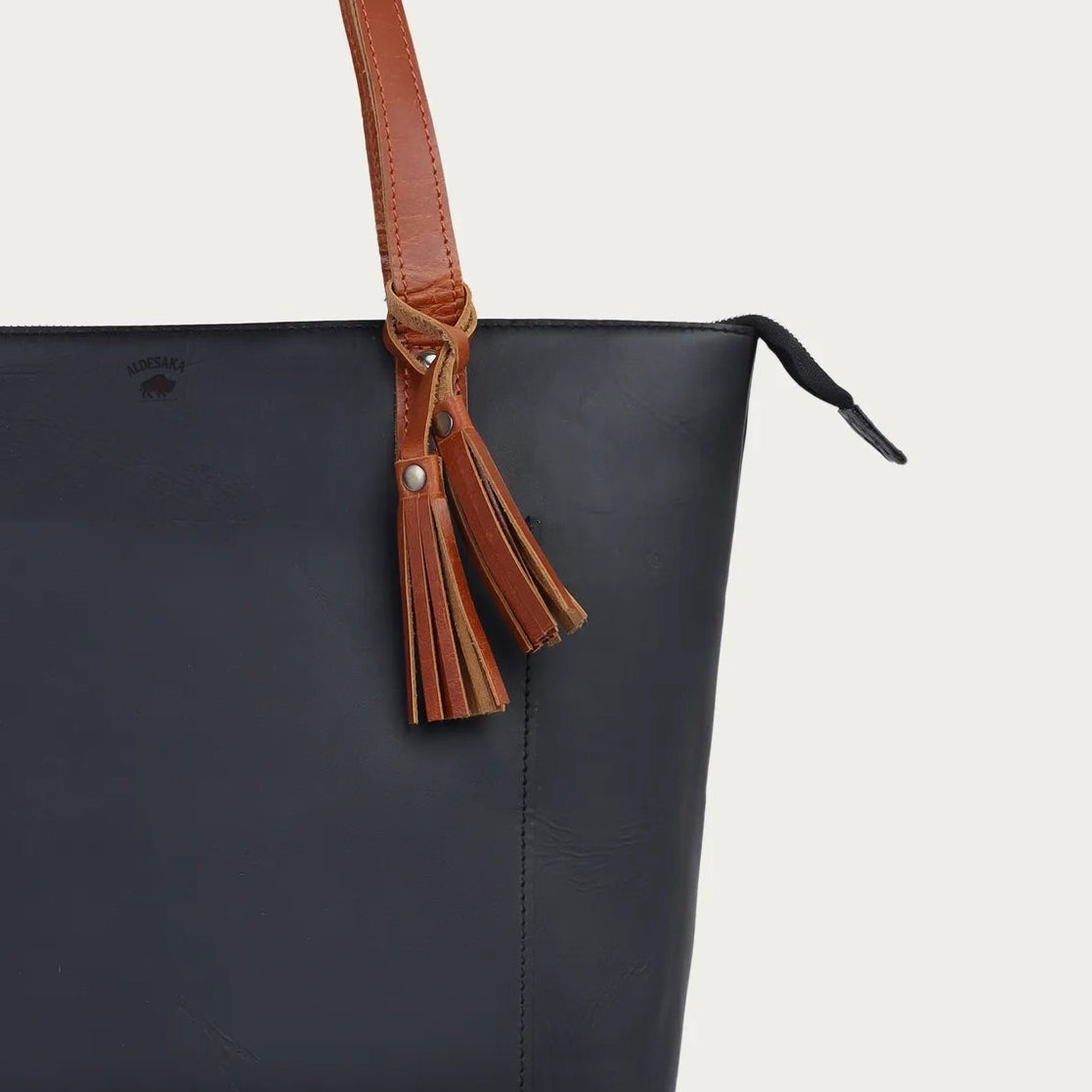Black tote bag with brown leather handle and strap on a light gray background