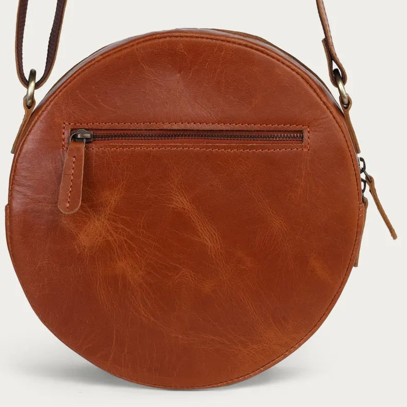 tan leather round bag with a strap on a light beige background