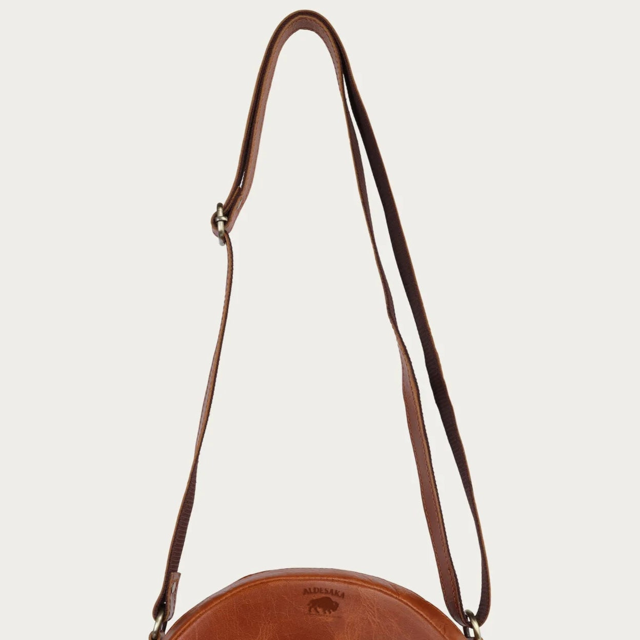 tan leather round bag with a strap on a light beige background