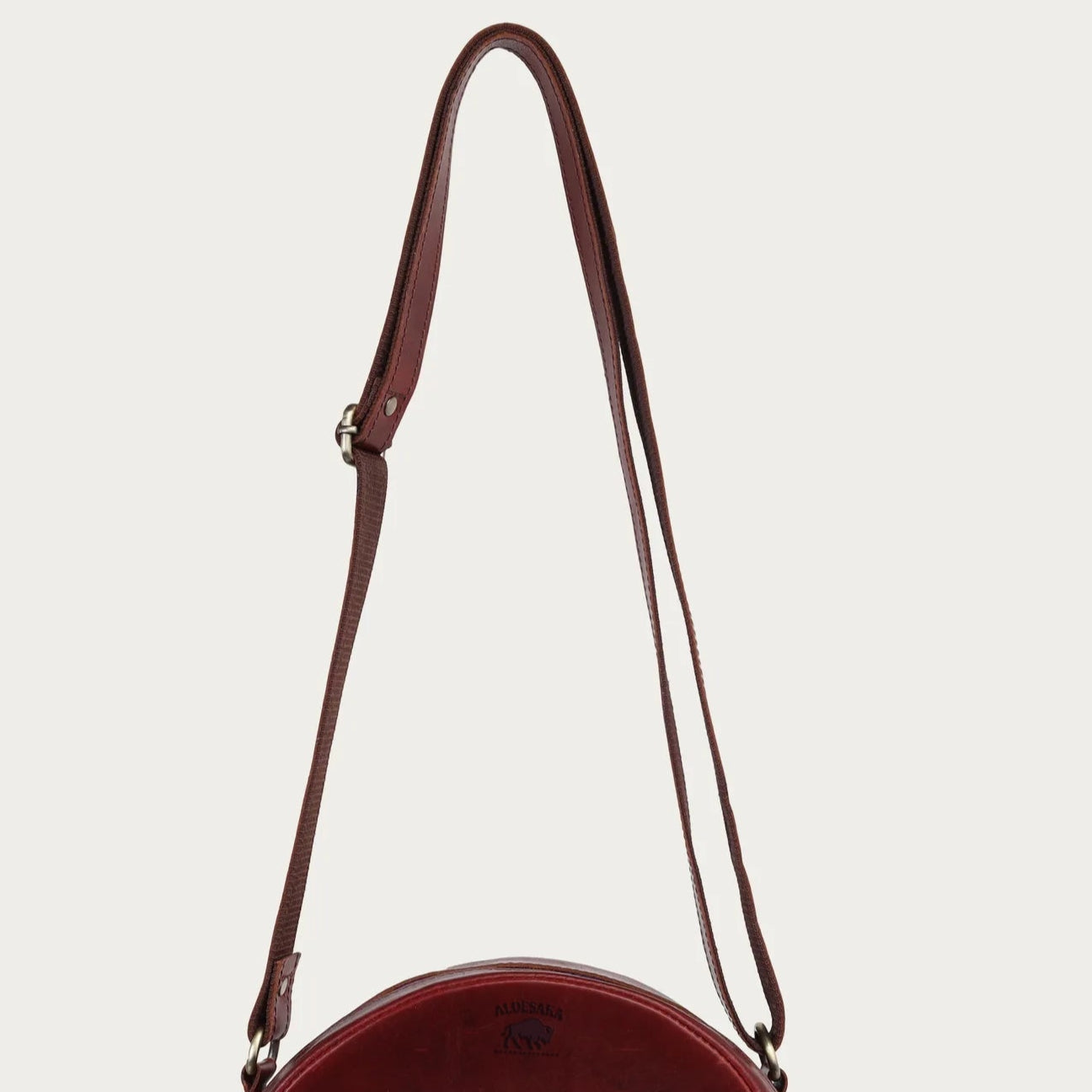Round wine leather bag with a brown strap on a light beige background